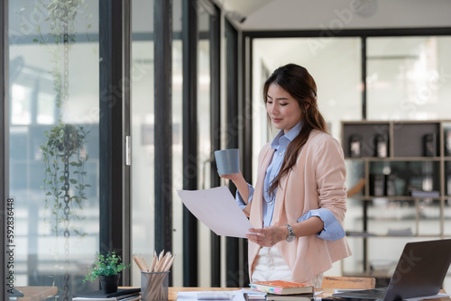 Asian businesswoman reading documents while drinking coffee in an office. photo