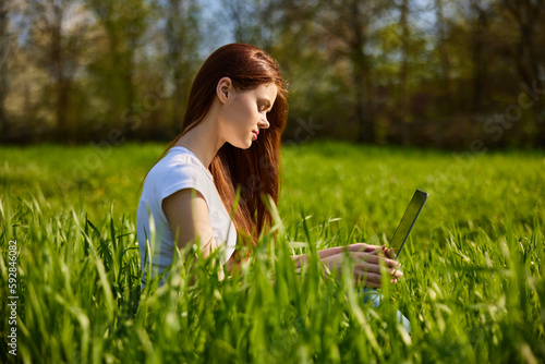 puzzled woman sitting in tall grass with laptop photo