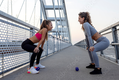 Two young athletic woman stretch and exercise before jogging on the bridge