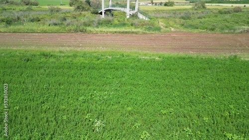 Aerial view of over a bridge above a creek in a green fields area