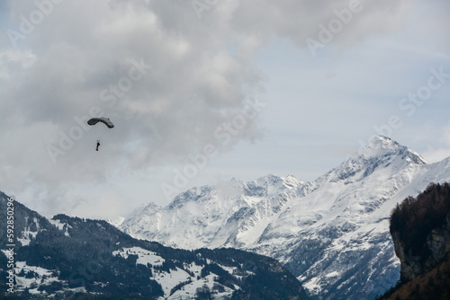 army paraglider close to landing in the swiss alps - in front of snow covered mountains