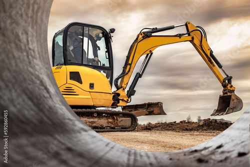 Mini excavator at the construction site on the edge of a pit against a cloudy blue sky. Compact construction equipment for earthworks. An indispensable assistant for earthworks. photo