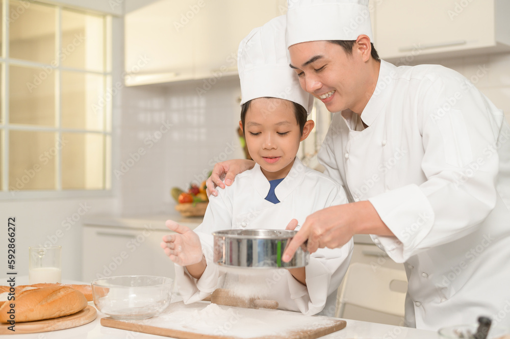 Young Asian father and his son wearing chef uniform baking together in kitchen at home Young Asian father and his son wearing chef uniform baking together in kitchen at home