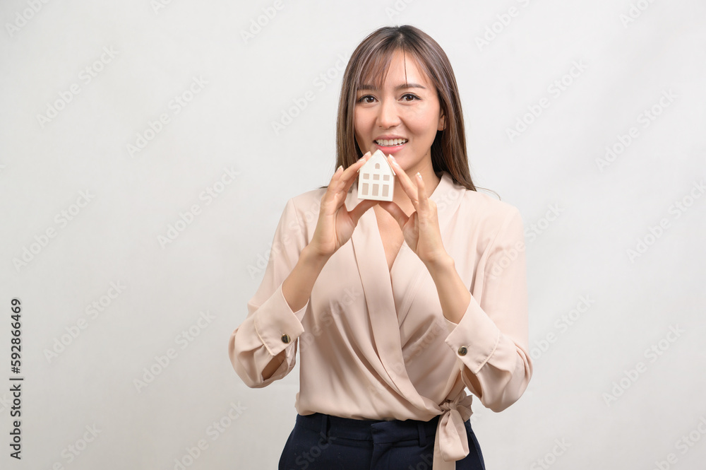 Young smiling woman holding small model house over white background studio. Young smiling woman holding small model house over white background studio.