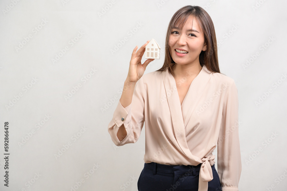 Young smiling woman holding small model house over white background studio. Young smiling woman holding small model house over white background studio.