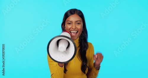 Happy, megaphone and cheering with Indian woman in studio for announcement, good news and vote. Change, speech and promotion with female on blue background for attention, ambassador and opinion photo