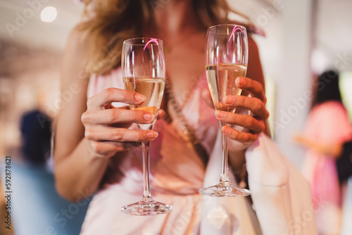 Woman in pink dress holding two glasses of champagne in the hands.