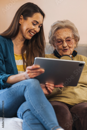 Granddaughter visiting her grandma, showing her pictures on tablet.