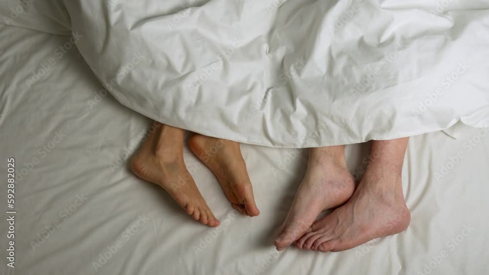 Female and male legs in a white bed under blanket Female and male legs in a white bed under blanket
