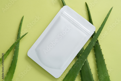 Unlabeled beauty mask sheet with Aloe vera leaves on pastel background. Aloe vera (Aloe barbadensis miller) flushing out the excess sebum, microbes, and dirt.
