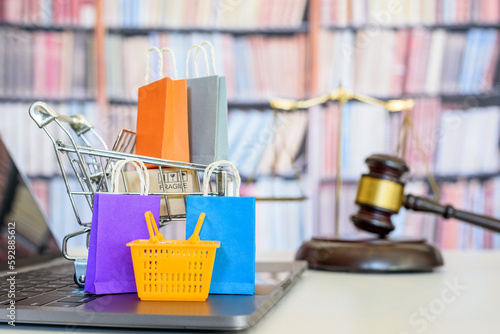 Consumer rights and consumer protection, business law concept : Shopping basket, shopping bags and  a shopping cart on a laptop computer with judge gavel, balance sale of justice and bookshelf behind.