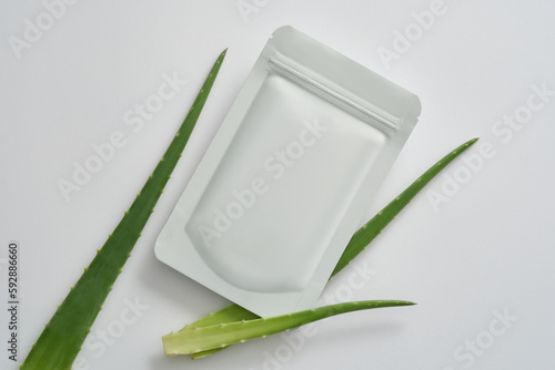 Minimal style for advertising cosmetics - mockup of a facial sheet mask package and aloe vera leaves on white background. Aloe vera has anti-aging effects, prevents wrinkles and stimulates collagen.