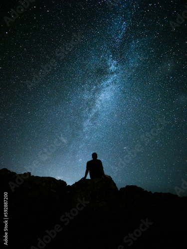 Persona sentada bajo las estrellas y la vía láctea en la montaña.
