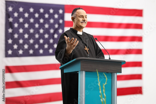Priest giving a speech on a podium in front of USA flag photo