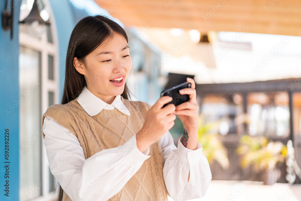 Fototapeta premium Young Chinese woman at outdoors playing with the mobile phone