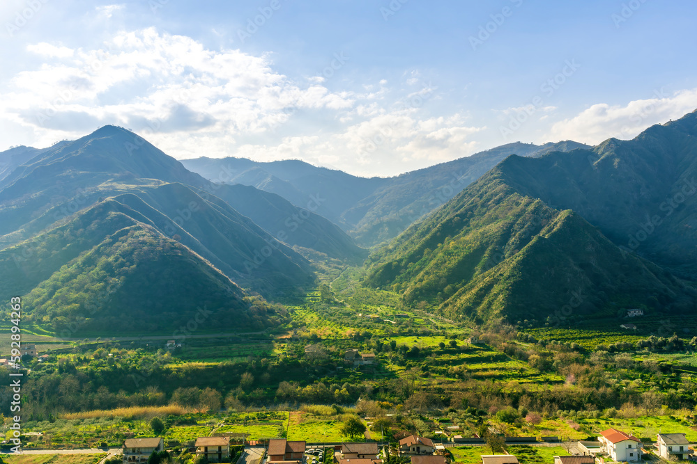 landscape of green summer highland mountain range with green beautiful valley with nice town below and amazing blue cloudy sky landscape of green summer highland mountain range with green beautiful valley with nice town below and amazing blue cloudy sky