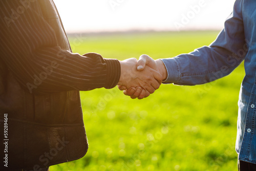 Negotiation. Two farmers agree by shaking hands in a green wheat field. The concept of agricultural business.