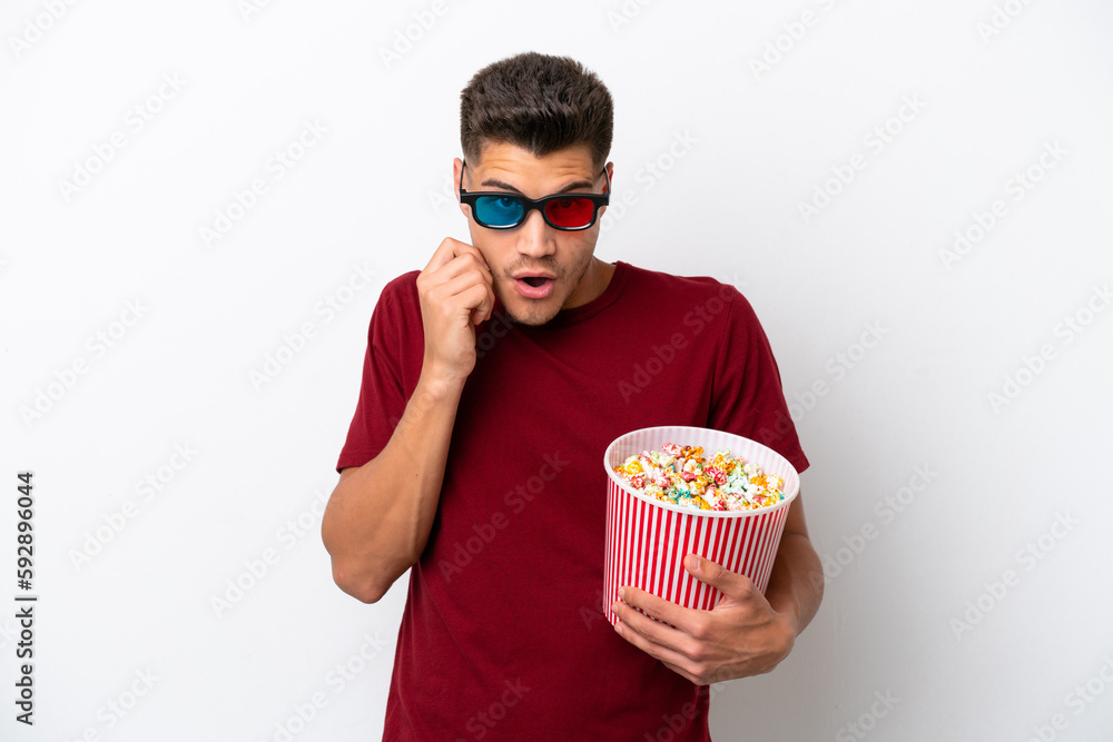Young caucasian man isolated on white background with 3d glasses and holding a big bucket of popcorns