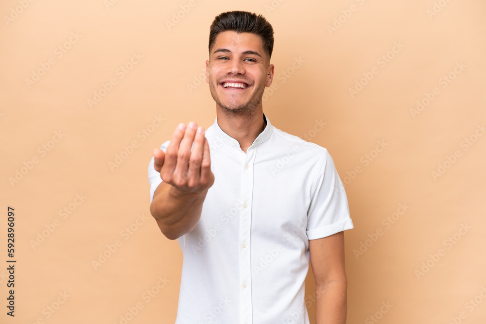 Young caucasian man isolated on beige background inviting to come with hand. Happy that you came Young caucasian man isolated on beige background inviting to come with hand. Happy that you came