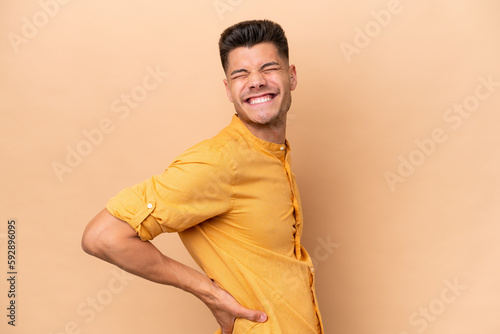 Young caucasian man isolated on beige background suffering from backache for having made an effort