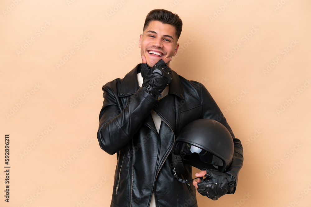 Fototapeta premium Young caucasian man with a motorcycle helmet isolated on beige background happy and smiling