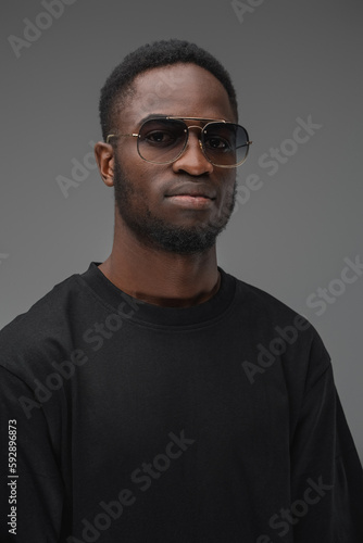 Shot of trendy black guy dressed in t shirt and sunglasses looking at camera.
