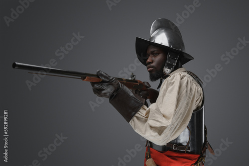 Shot of medieval soldier dressed in steel armor and helmet aiming flintlock musket.