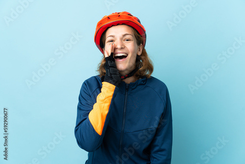Young cyclist woman isolated on blue background shouting with mouth wide open