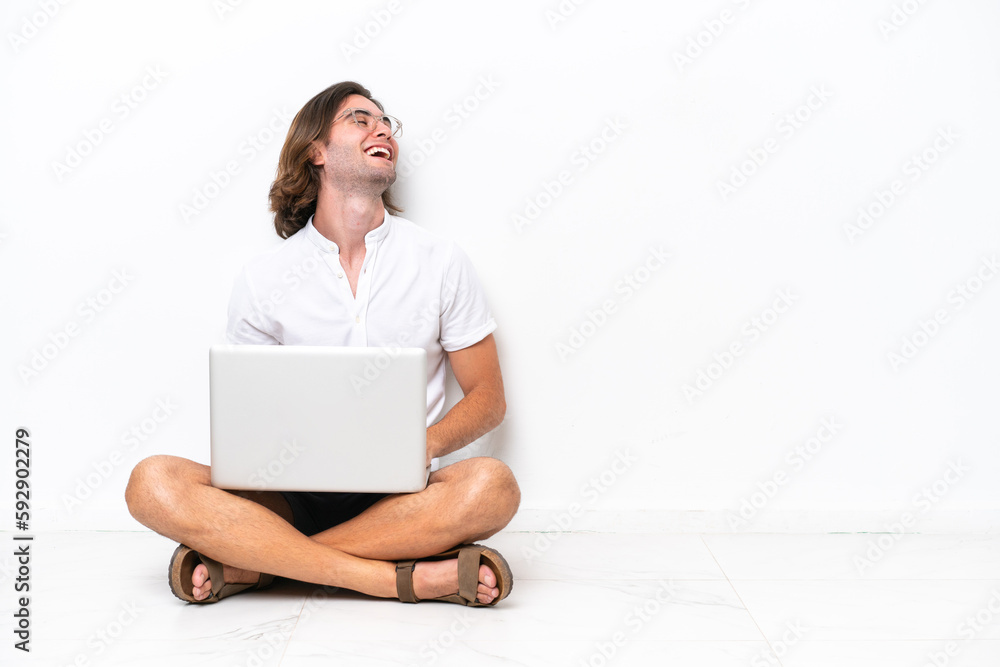 Young handsome man with a laptop sitting on the floor isolated on white background laughing in lateral position Young handsome man with a laptop sitting on the floor isolated on white background laughing in lateral position
