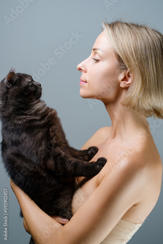 Studio portrait of young blode woman and her adorable black tabby cat.