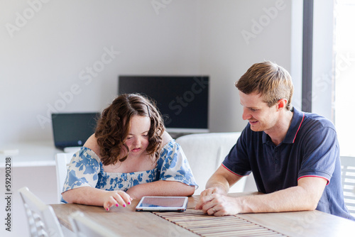Male NDIS provider assisting young woman with down syndrome using tablet photo
