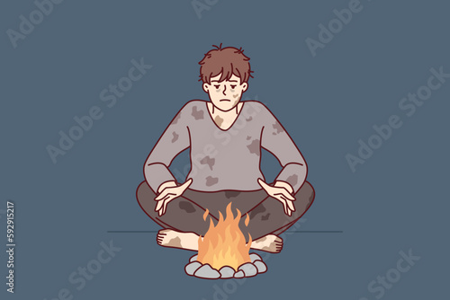 Homeless man in dirty clothes warms hands sitting by fire trying to survive due to lack of own home. Homeless guy needs help from social services and benefits or food stamps after losing job 