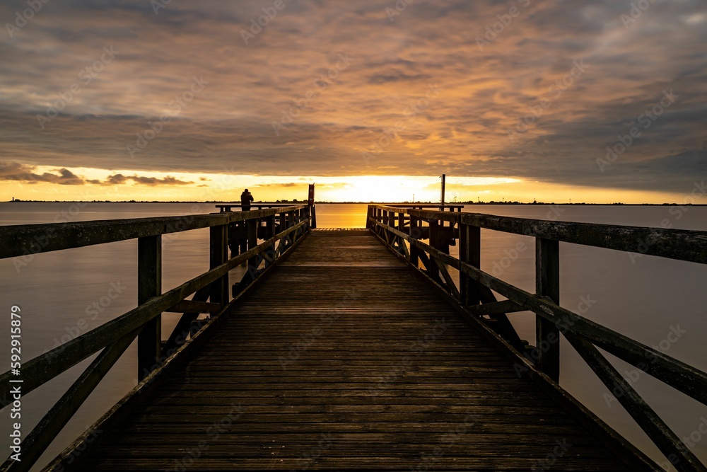 Pier leading to a calm sea under the golden glow of sunset in a cloudy sky
