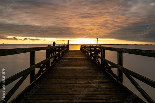 Fototapeta Naklejka Na Ścianę i Meble -  Pier leading to a calm sea under the golden glow of sunset in a cloudy sky