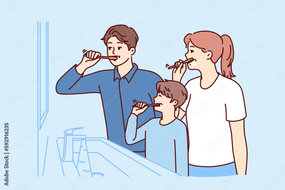 Family brushes teeth together standing in bathroom near mirror to teach boy morning hygiene procedures. Mom and dad with son use toothbrushes to clean mouth after eating to avoid teeth caries Family brushes teeth together standing in bathroom near mirror to teach boy morning hygiene procedures. Mom and dad with son use toothbrushes to clean mouth after eating to avoid teeth caries
