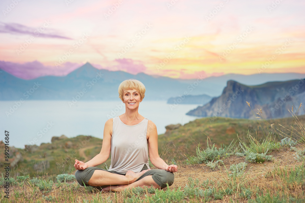 Senior woman doing yoga exercises with mountain sunset on the background