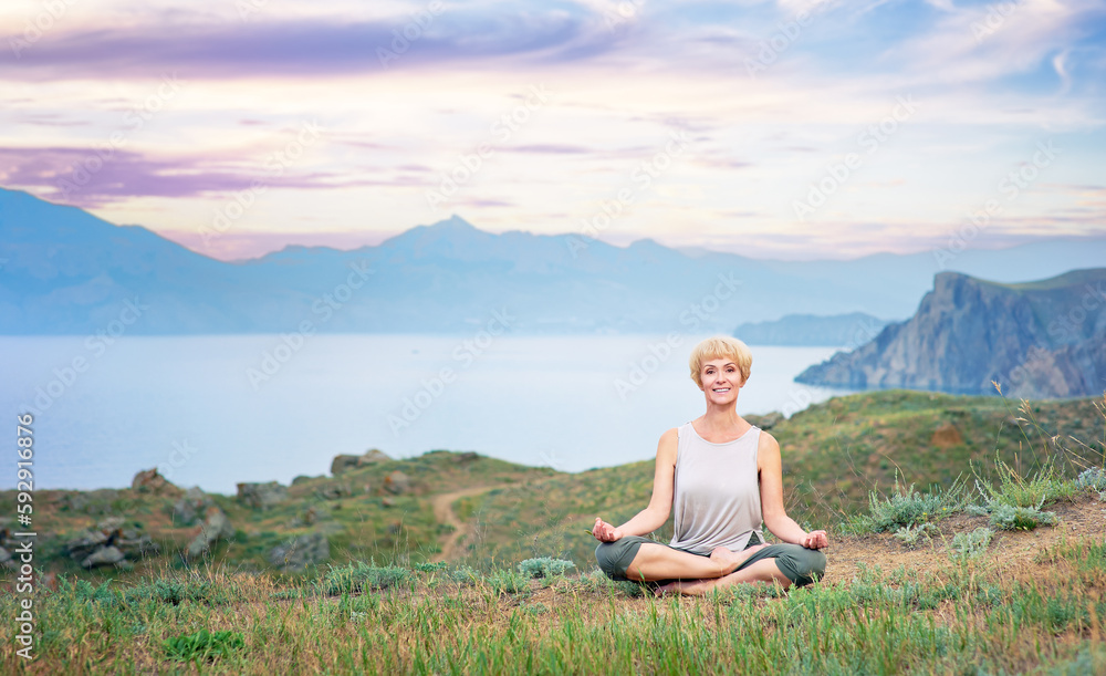 Senior woman doing yoga exercises with mountain sunset on the background