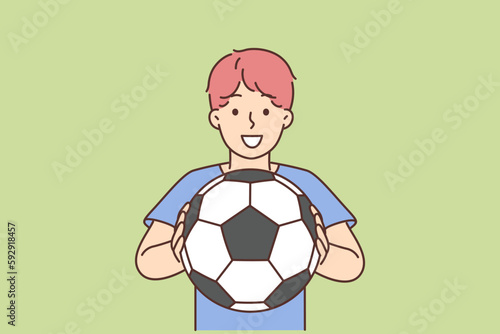 Cheerful boy of school age holding soccer ball and smiling offers to play football