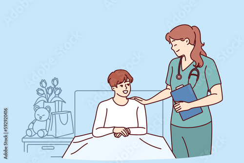 Woman doctor near boy lying on bed in hospital after complications of chronic disease. Doctor pediatrician supports teenager undergoing rehabilitation in hospital after complex operation 