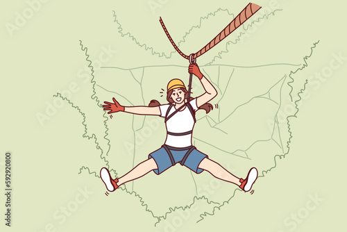 Woman tourist hangs on zip line over forest cliff enjoying extreme vacation in picturesque place. Tourist girl descends from mountain on rope getting adrenaline from adventures while traveling 