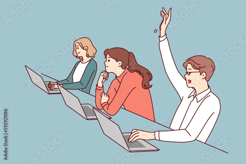 Man student sitting at desk with laptop raises hand to attract attention of teacher and ask question on topic of lecture. People listening to lecture in college or university auditorium 