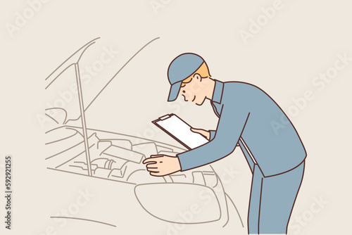 Man auto mechanic with clipboard conducts technical inspection of car standing near open hood 