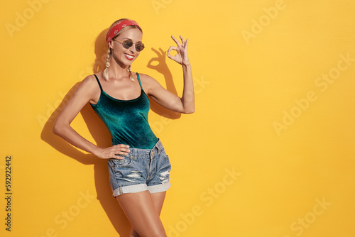 Very good! Young pretty smiling woman showing OK sign against yellow wall.