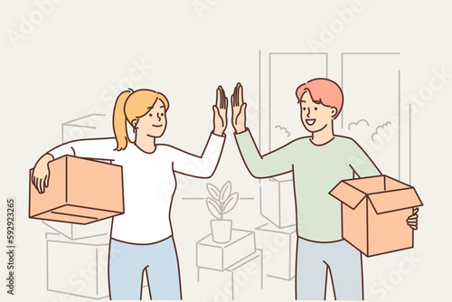 Happy married couple moving into new house and giving each other high five standing with boxes