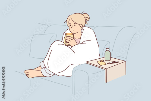 Woman sick with flu wrapped in blanket sits on couch and drinks hot decoction of herbs