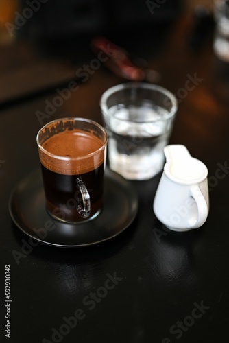 Black table with a cup of coffee, a portion of milk and a cup of water