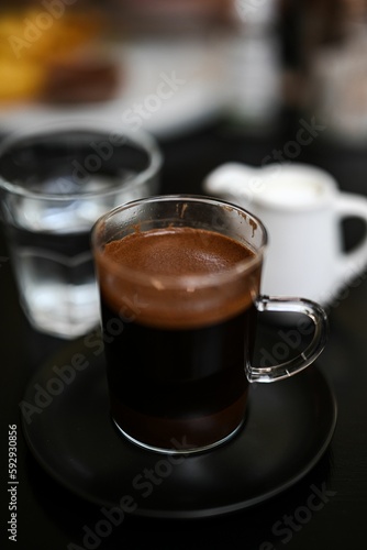 Vertical shot of Greek coffee in a transparent glass with a blurry background in a restaurant