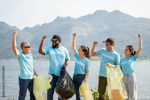 Happy Group of young volunteers helping to keep nature clean and picking up the garbage from a sandy shore.