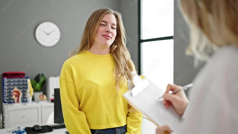 Young blonde woman doctor and patient having medical consultation writing medical report at clinic Young blonde woman doctor and patient having medical consultation writing medical report at clinic