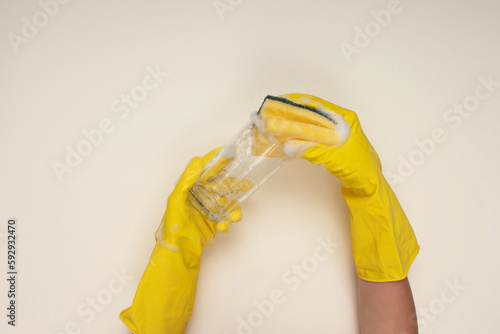 woman wearing yellow cleaning gloves on light color background cleaning glass cup with cleaning sponge